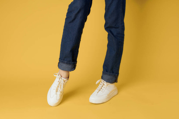 Fashionable shoes white sneakers legs yellow background cropped view - Фото, зображення