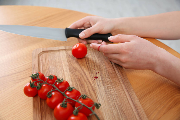 Woman cut finger with knife while cooking at wooden table, closeup - Foto, Imagen
