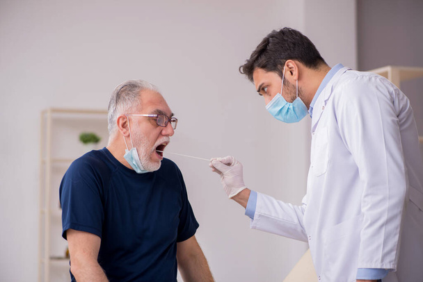 Vieux patient de sexe masculin visitant jeune médecin masculin otorhinolaryngologis - Photo, image