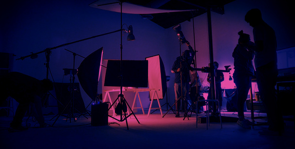 ネオンブルーピンクのカラー撮影。大きなスタジオに設置されたビデオ制作の舞台裏です。シルエットでクルーチーム作業やカメラ機器。映画製作業。照明設置. - 写真・画像