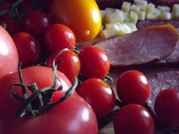 gesneden gerookte worst van vier rassen met kaas en rode en gele tomaten en kerstomaten - Foto, afbeelding