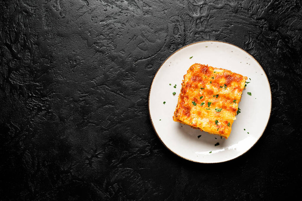 Egy adag darált marhahús lasagne tetején olvadt sajttal és díszített friss petrezselyemmel tálalva szürke tányéron. Kiváló kilátás. hely az sms-nek. fekete háttér - Fotó, kép