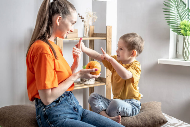 A happy mother in a playful way is teaching her little son to count using fruits. Concept of family, pastime and activities with the child. - Photo, image