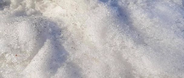 Baharın başında donmuş buzla birlikte kirli kara yakın plan. Kar dokusu üzerindeki güneş ışığı ve gölgeler, iklim ve mevsimsel hava kavramı. - Fotoğraf, Görsel