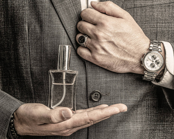 Αρσενικό που κρατάει άρωμα μπουκαλιού. Χέρι με ρολόι χειρός σε ένα επαγγελματικό κοστούμι. Άρωμα ή κολόνια μπουκάλι και αρωματοποιίας, καλλυντικά, άρωμα μπουκάλι κολόνια, αρσενικό εκμετάλλευση κολόνια - Φωτογραφία, εικόνα