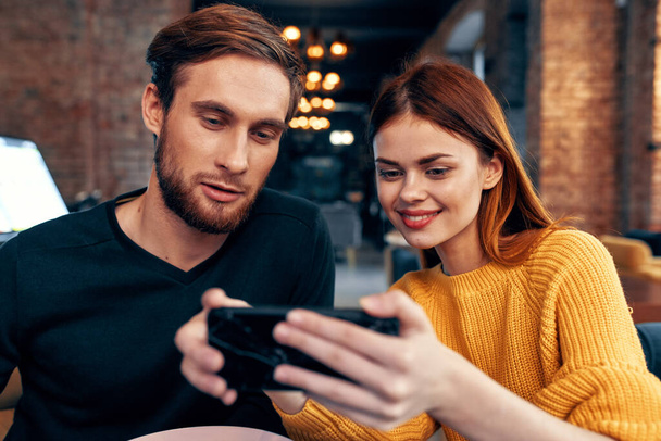 jovem casal homem e mulher em um restaurante encomendar comida e telefone celular na iluminação mão - Foto, Imagem