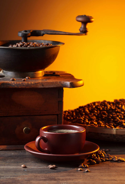 Taza de café negro, molinillo de café y frijoles asados en una mesa de madera vieja. - Foto, Imagen