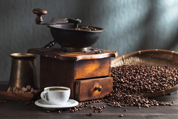 Egy csésze fekete kávé, kávéfőző és sült bab egy régi fa asztalon.. - Fotó, kép