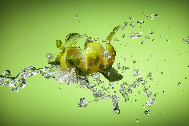 Frische Limette, Minze und Eis im Spritzer auf grünem Hintergrund. - Foto, Bild