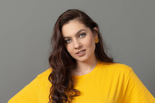 portrait of a young teenager with long wavy hair dressed in a yellow t-shirt, isolated on gray  - Fotografie, Obrázek