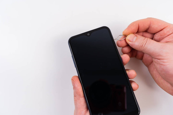 las manos de los hombres insertan una tarjeta SIM en un teléfono inteligente usando una tecla de clip - Foto, Imagen