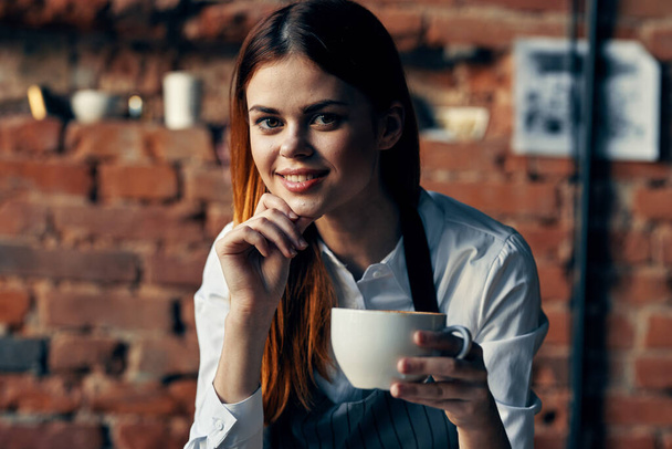 όμορφη γυναίκα σερβιτόρο κύπελλο με ποτό καφέ τούβλο τοίχο - Φωτογραφία, εικόνα