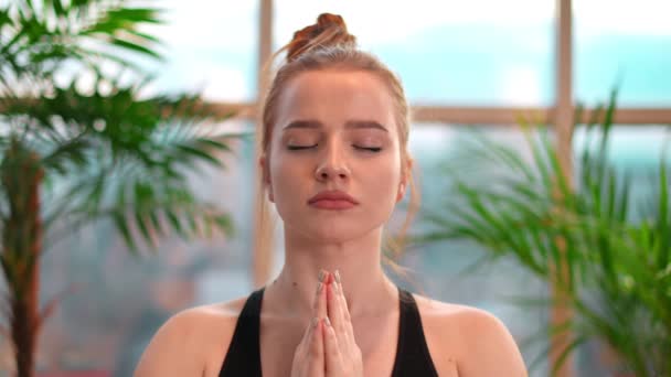 Young woman in yoga prayer pose meditating indoors in apartment. City on background. - Footage, Video