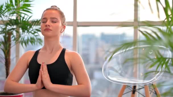 Yoga yapan genç bir kadın evde meditasyon yapıyor. Arkaplanda şehir. - Video, Çekim