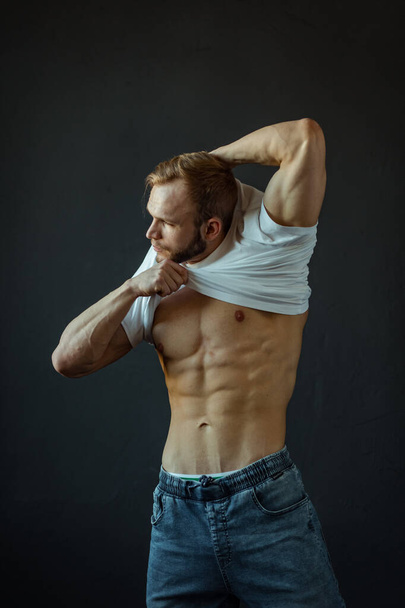A young Man of strong constitution with a relief figure of a bodybuilder with a beautiful torso. Shooting in the studio on a black background. - Valokuva, kuva