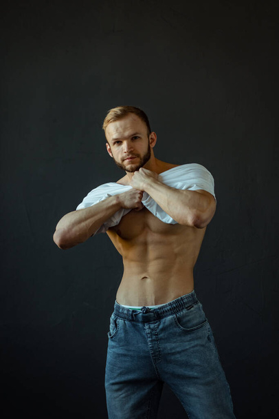 A young Man of strong constitution with a relief figure of a bodybuilder with a beautiful torso. Shooting in the studio on a black background. - Valokuva, kuva