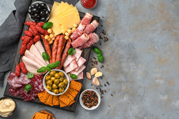 Hunting sausages, salami, bacon, ham, various types of cheese, olives and spices on a cutting board on a gray background. Sliced meat, appetizer. - Foto, afbeelding