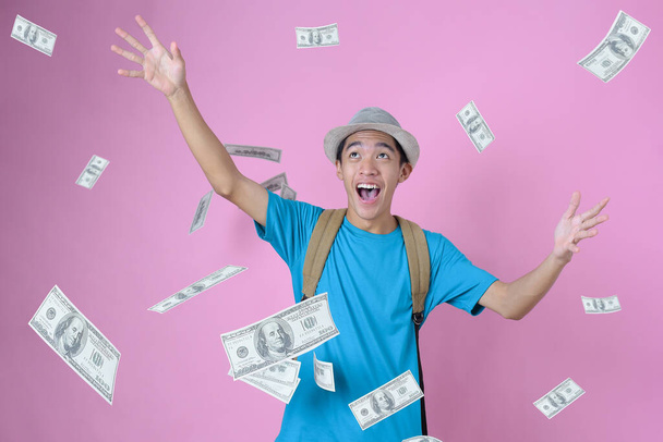 feliz joven asiático viajero hombre soñando tener mucho dinero, soñando dinero cae desde el cielo, contra en rosa fondo - Foto, Imagen