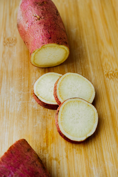raw sweet potato tuber and slices on a chopping wooden board. cooking homemade simple food, Yam recipes . vertical food content, selective focus - Foto, afbeelding