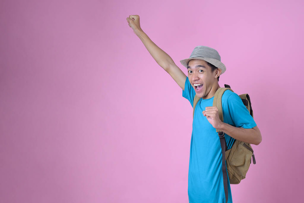 Retrato de atractivo joven alegre turista asiático viajeros con mochila y sombrero con gesto de vuelo aislado sobre fondo rosa - Foto, imagen