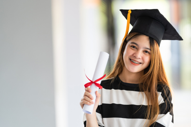 Fiatal ázsiai nő egyetemi diplomások ballagási köntös és habarcs rendelkezik diploma tanúsítvány ünnepli az oktatás teljesítményét az egyetemi campus. Oktatási állomány fényképe - Fotó, kép