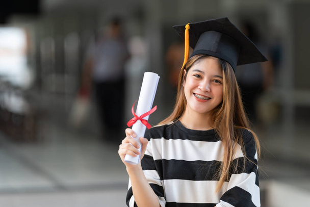 Молодая азиатка, окончившая университет в выпускном платье и на минометах, имеет диплом о получении образования в университетском городке. Фондовое фото - Фото, изображение
