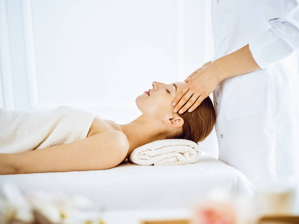 Beautiful woman enjoying facial massage with closed eyes in spa center - Photo, Image