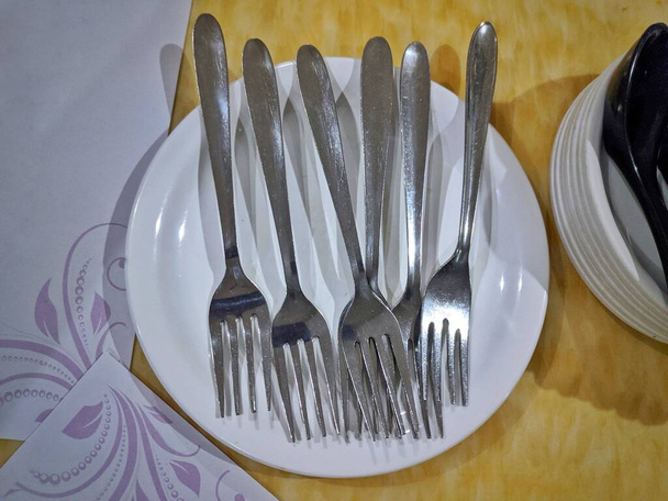 Hyderabad Indie - 10. března 2021: pár ocelových vidlic na bílém talíři ve žlutém pozadí - Fotografie, Obrázek