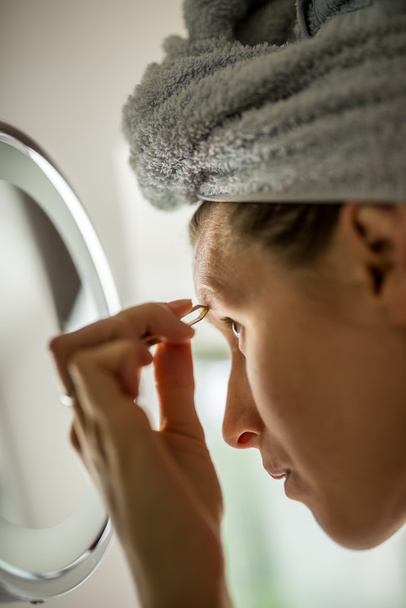 Woman plucking her eyebrows in the mirror - Φωτογραφία, εικόνα