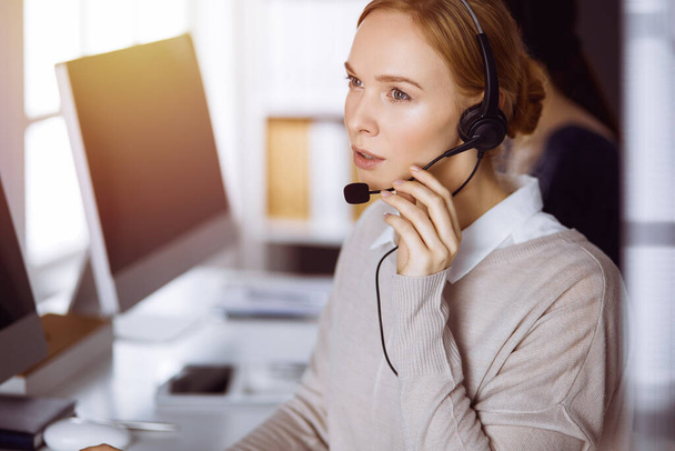 Businesswoman talking by headset in office. Call center and diverse people group in business - Foto, Imagem