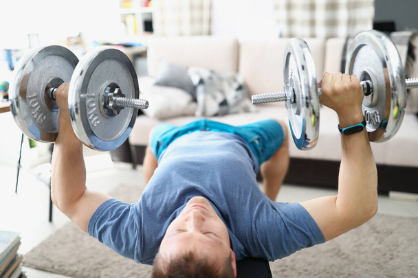Young man doing exercises with heavy dumbbells for muscles of biceps - Foto, Imagen