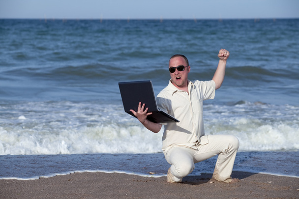 Angry man punching laptop at the beach - Fotó, kép