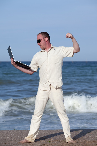 Sunburnt businessman at the beach punching his laptop - Fotó, kép