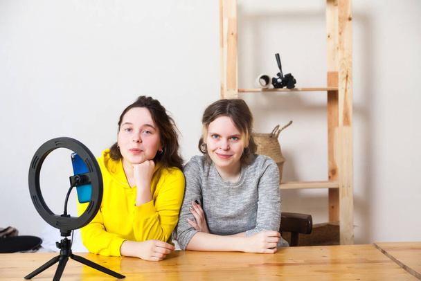 Twee 15-jarige vrouwelijke bloggers leiden live uitzending en lichten zichzelf op met ringlamp in light roo - Foto, afbeelding
