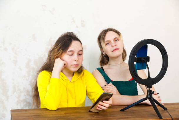 Κορίτσια ηλικίας 16 ετών καταγράφουν βίντεο σε smartphone και ανάβουν μόνοι τους με λάμπα δακτυλίου στο τραπέζι σε light roo - Φωτογραφία, εικόνα