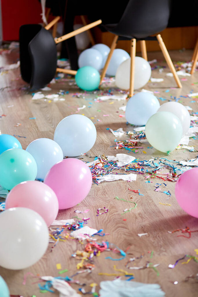 Na feestchaos, rommelig in de woonkamer thuis, tafel met pizza en champagneglazen bedekt met confetti en ballonnen, stoel op de vloer 's morgens na feestviering. - Foto, afbeelding