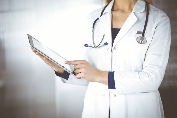 Une femme-médecin inconnue tient un ordinateur tablette dans ses mains, alors qu'elle se tient dans une clinique. Médecine avec un stéthoscope dans son bureau, gros plan. Service médical parfait dans un hôpital. Médecine - Photo, image