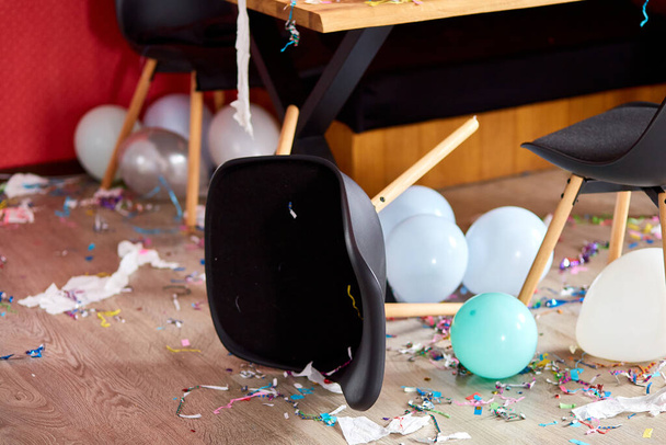 Po party chaos, chaotický v obývacím pokoji doma, stůl s pizzou a šampaňské sklenice pokryté konfety a balónky, židle na podlaze v dopoledních hodinách po party oslavy. - Fotografie, Obrázek