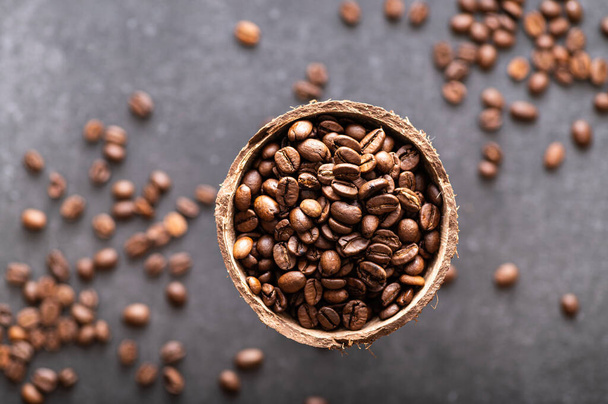 black coffee beans arabica, aromatic in a coconut dish, sprinkled beans on the table, close-up, top view - Zdjęcie, obraz