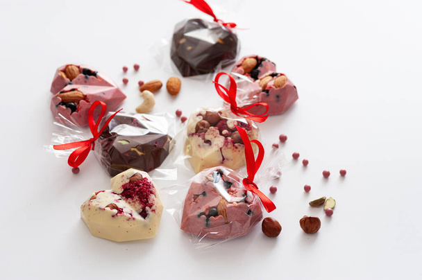 μείγμα σοκολατάκια, σε μορφή καρδιάς με ροζ, γάλα και λευκή σοκολάτα με φράουλες, μύρτιλλα και αμύγδαλα, δεμένο με κορδέλα, χειροποίητη, πάνω όψη, σε λευκό φόντο - Φωτογραφία, εικόνα