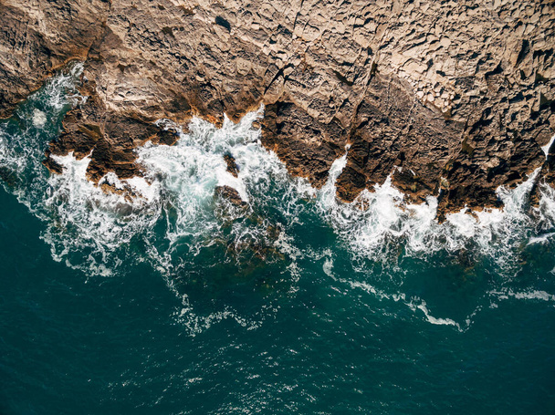 Hava aracı, güzel okyanus dalgalarının en üst görüntüsü kayalık bir adanın kıyısına çarpıyor.. - Fotoğraf, Görsel