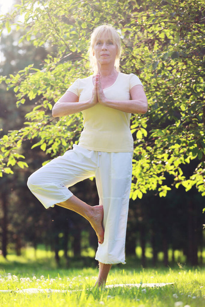 Beautiful mature woman practice yoga in summer park - Foto, Bild