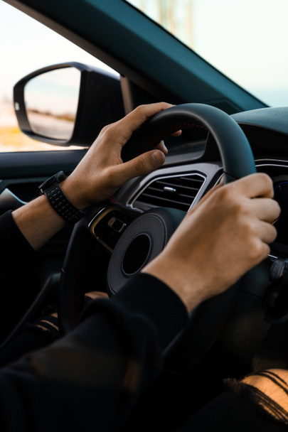 Zbliżenie rąk trzymających kierownicę samochodu, noszących inteligentny zegarek na nadgarstku. W ciemnych, nowoczesnych ubraniach.. - Zdjęcie, obraz