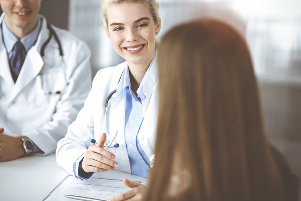 Woman-doctor with male colleague are consulting patient woman while sitting at the desk in modern clinic. Perfect medical service, medicine concept - Photo, image