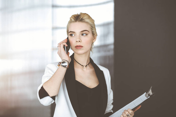 Young blonde business woman or female student in white suit is standing in modern office. Lifestyle and diverse people concept - Fotografie, Obrázek