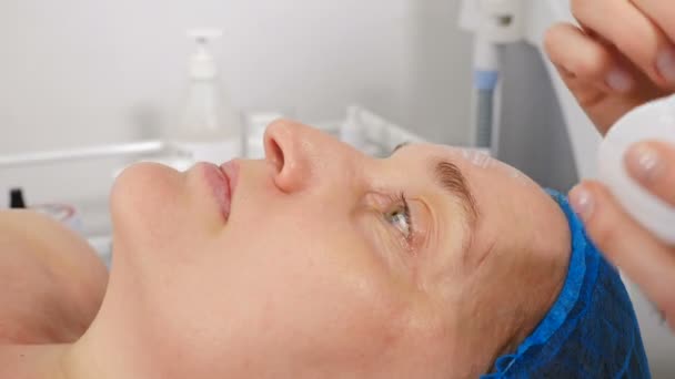Концепция клиники красоты. Пожилая женщина проходит процедуру по уходу за лицом. Косметик распыляет кремовую маску на лицо пожилой женщины кисточкой. Концепция обновления лица. Вид сбоку. 4 k видео - Кадры, видео