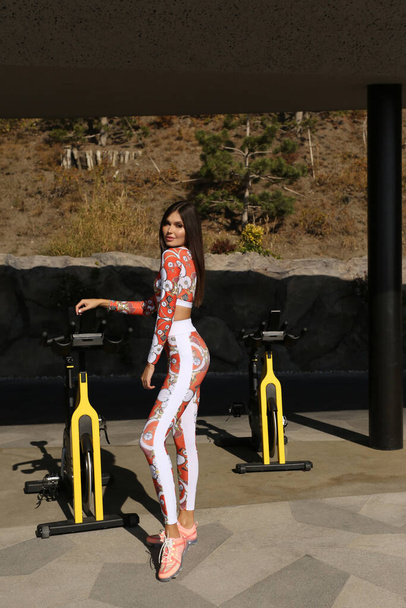 fashion photo of beautiful sexy woman with dark hair in elegant sportive clothes posing in outdoor gym - Valokuva, kuva