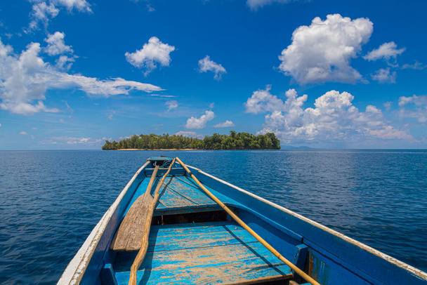 синій човен посеред моря перед невеликим островом з блакитним небом і хмарами
. - Фото, зображення