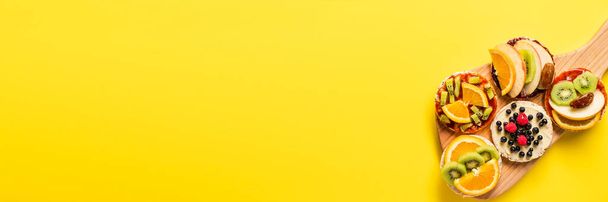 Crispy puffed rice cakes on board with fresh fruit kiwi banana apple blueberries raspberries and orange on the yellow background - top view on healthy organic vegetarian or vegan breakfast gluten free - Фото, изображение