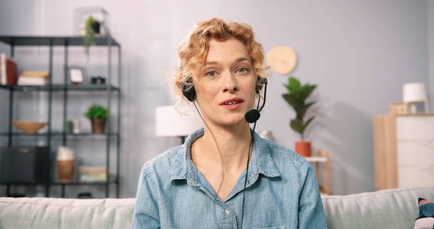 Headshot portrait view of young caucasian woman in headset talking on video call at home. Female coach or tutor in headphone having online webcam conference or virtual digital web conversation - Zdjęcie, obraz
